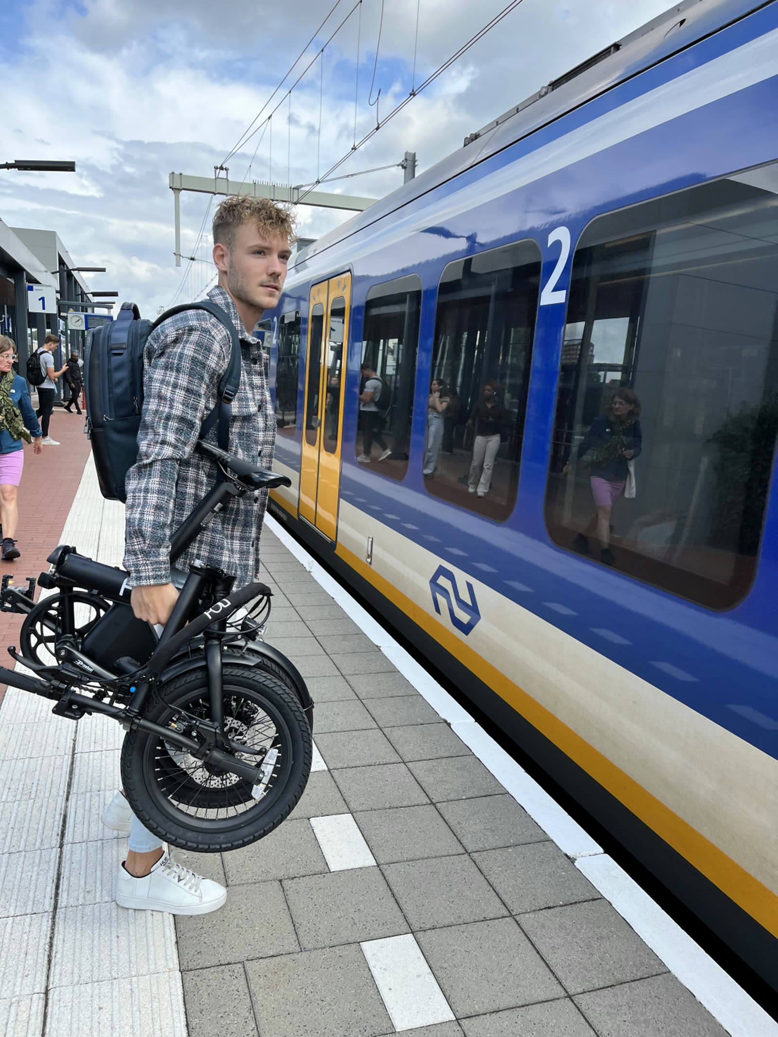 Reiziger draagt een opgevouwen FOLT vouwfiets langs de trein over het perron